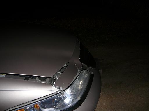 Damaged silver car hood and headlight at night