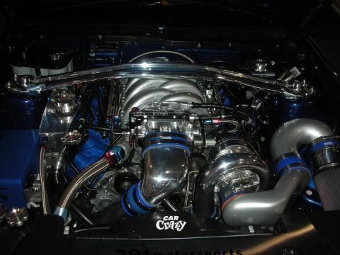 1998 Ford Crown Victoria - show-detailed engine bay with a polished supercharger, blue silicone hoses and a Car Crazy plaque under bright lighting.