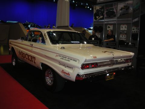 1998 Ford Crown Victoria - white vintage two-door coupe lettered 'the Rocket' with chrome wheels parked on display at an indoor automotive show.