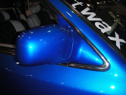 1998 Ford Crown Victoria - body-colored blue side mirror on a glossy car with partial 'wax' lettering visible on the window behind it.