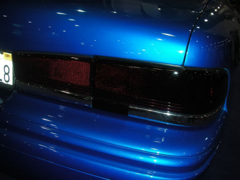 1998 Ford Crown Victoria - Smoked blacked-out taillights on the rear of a deep blue custom car beside a yellow plate showing the number 8.