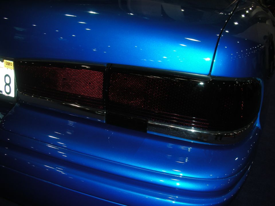 Blacked-out taillights on a glossy blue car with a yellow plate reading 8