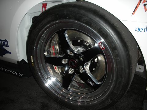 1998 Ford Crown Victoria - black-and-polished five-spoke wheel wrapped in a wide drag slick under the fender of a white graphics-wrapped car.