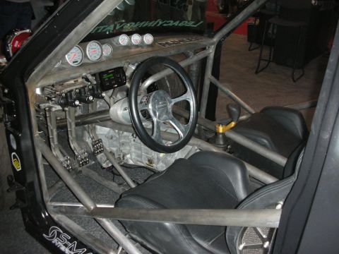 1998 Ford Crown Victoria - Interior of a tube-frame race car with full roll cage, cluster of round gauges, small steering wheel and black bucket seats.