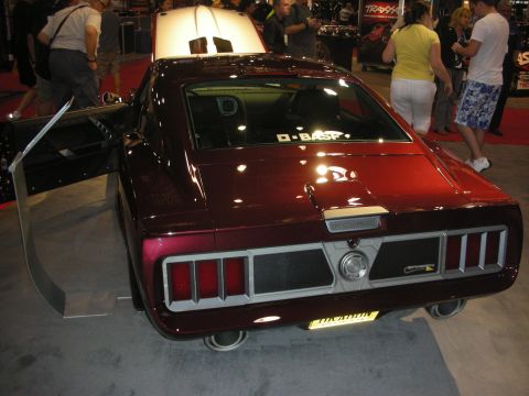1998 Ford Crown Victoria - deep maroon custom fastback coupe shown rear three-quarter with slatted taillights amid crowds at an indoor show.