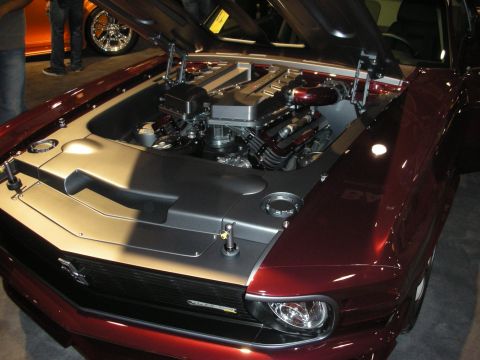 1998 Ford Crown Victoria - modern DOHC engine with a smooth cover sits under the open hood of a maroon custom muscle car at a show.