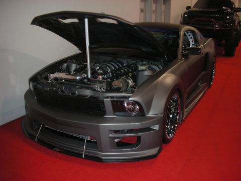 1998 Ford Crown Victoria - matte gray modified sports coupe sits with its hood raised on a red carpet, showing a custom front splitter and black mesh wheels.