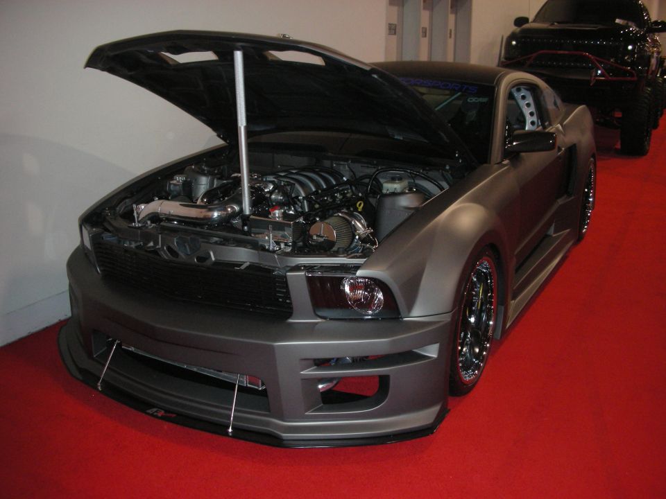 Matte gray modified coupe with hood up and front splitter on red show floor