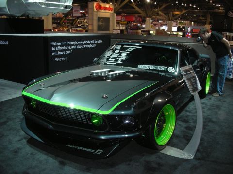 1998 Ford Crown Victoria - black widebody fastback muscle car with green pinstriping and green wheels displayed under spotlights at an indoor show.