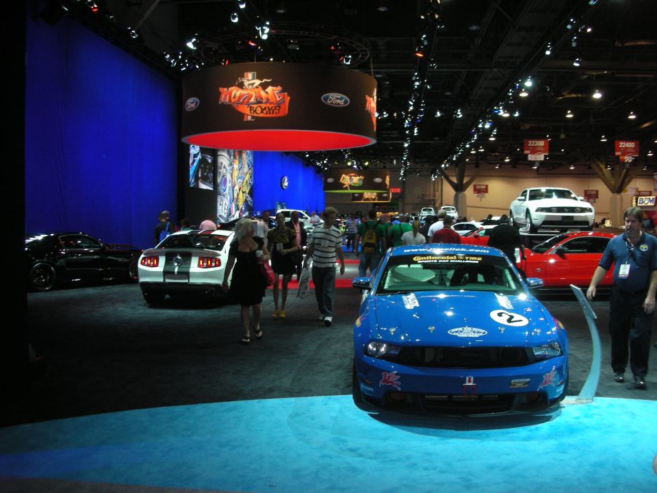 Indoor auto show floor with blue race coupe and crowd of attendees