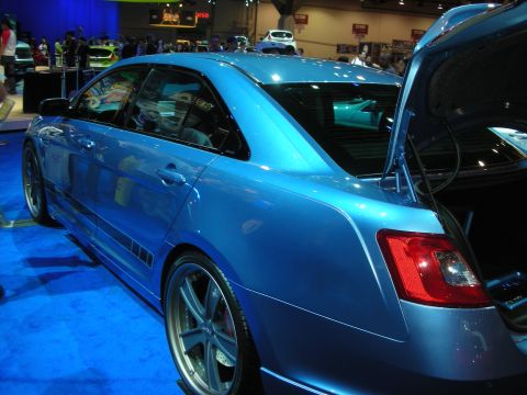 1998 Ford Crown Victoria - blue full-size sedan shown rear three-quarter with its trunk open and aftermarket wheels on a blue carpeted display stand.