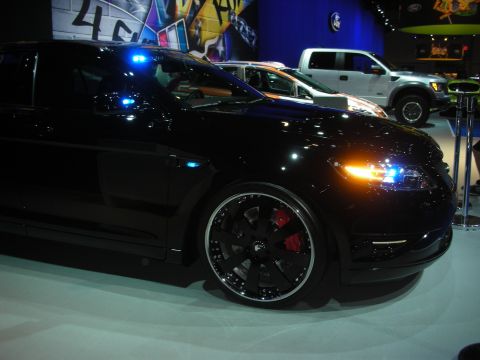 1998 Ford Crown Victoria - Side profile of a lowered black sedan with gloss-black multi-spoke wheels and red brake calipers, a Ford pickup behind it.