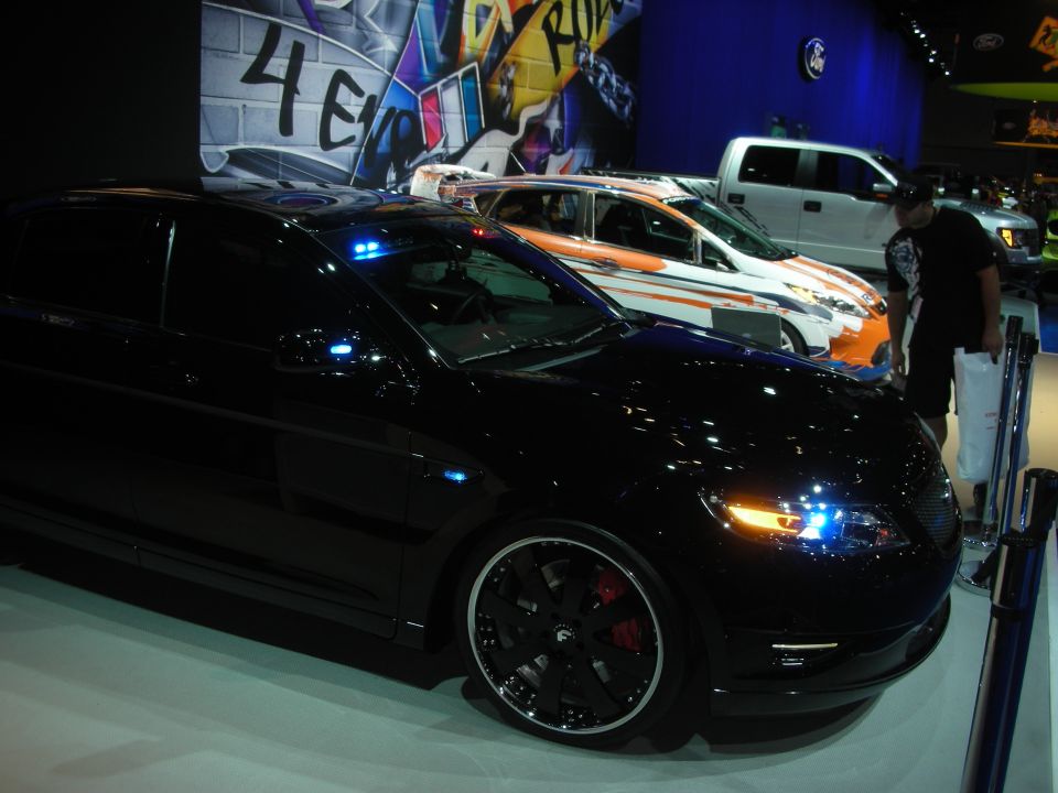 Black sedan front three-quarter with graffiti wall and pickup behind