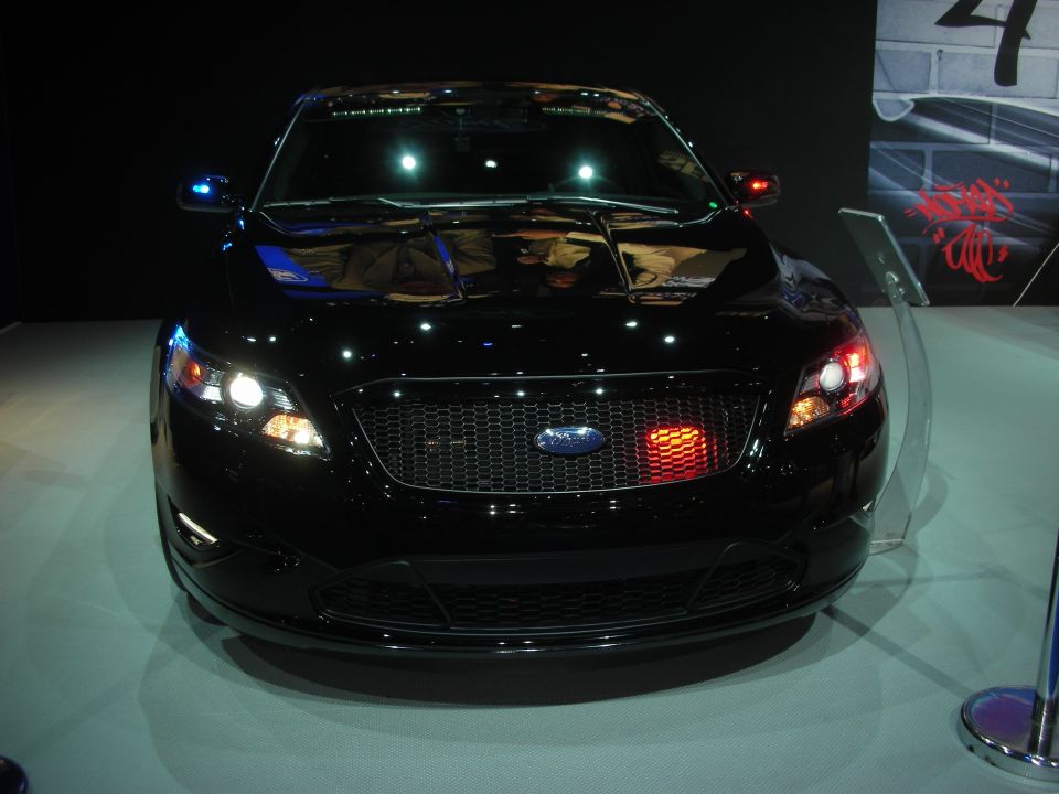 Front view of black Ford sedan with mesh grille on lit show stand