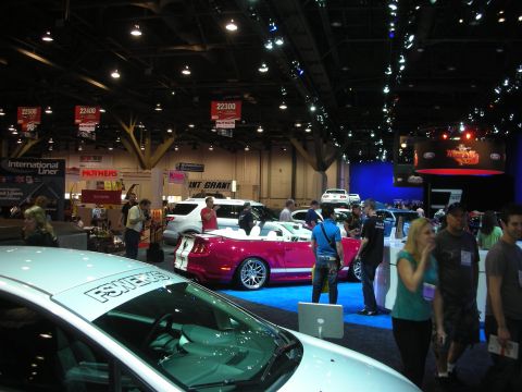 1998 Ford Crown Victoria - Visitors walk the floor of a large indoor automotive expo where a pink convertible and several other vehicles are displayed under banner nu…