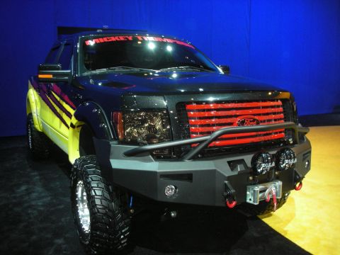 1998 Ford Crown Victoria - black and yellow custom Ford pickup truck with a heavy front bumper, winch, off-road tires and a colorful banner across the windshield.