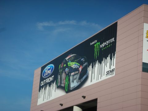 1998 Ford Crown Victoria - large building-mounted billboard reading Ford Out Front showing a rally car with Monster Energy branding against a blue sky.