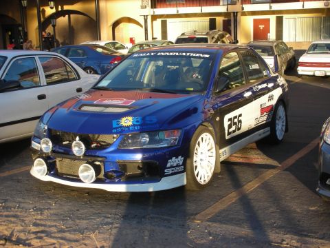 1998 Ford Crown Victoria - blue Mitsubishi Lancer Evolution rally car with number 256, white wheels and E85 ethanol sponsor graphics parked in a lot.
