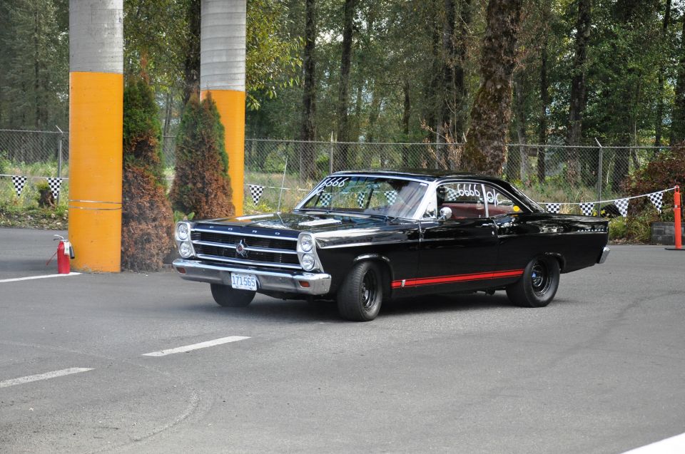 Black 1960s two-door muscle car with red stripe parked in a paved lot