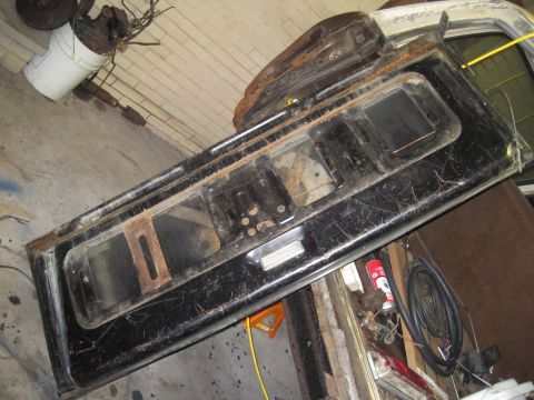 1979 Ford Bronco - A weathered black tailgate, likely from an older vehicle, is shown indoors with various tools and supplies nearby.