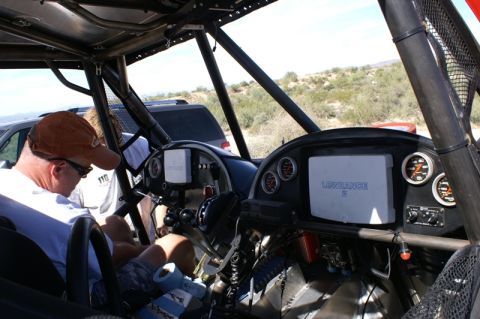 1990 Ford Bronco - Cockpit of an off-road race car with a steering wheel, gauges and a Lowrance navigation screen, a driver seated at left.