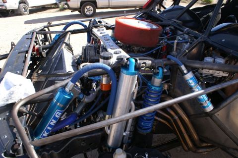 1990 Ford Bronco - Detail of an off-road race car's rear engine and suspension area showing blue coilover shocks and braided hoses.