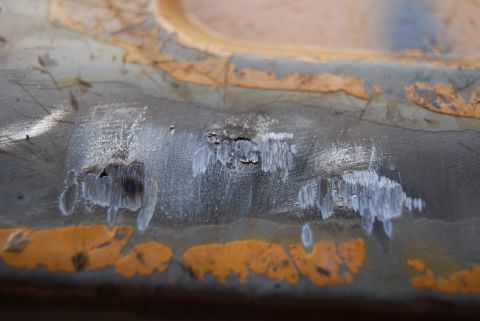 1982 Ford Bronco - This is a close-up view of damaged and rusted metal, showing areas where paint has chipped away.