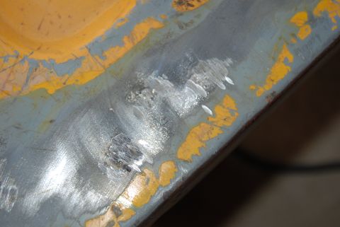 1982 Ford Bronco - A close-up view of a damaged metal panel reveals underlying welds and chipped paint, suggesting repair work.