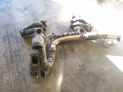 1995 Ford Probe - This is an exhaust manifold and downpipe assembly, likely from a vehicle, lying on a concrete surface.