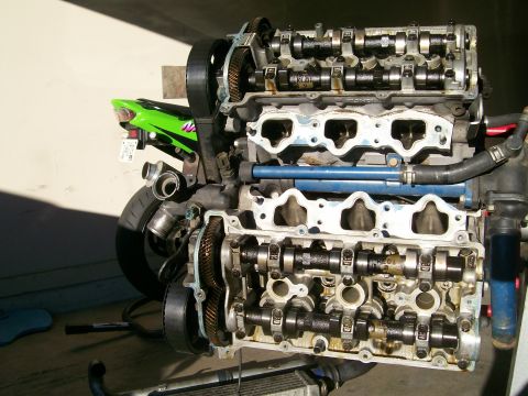 1995 Ford Probe - Engine block with exposed camshafts and gears, green motorcycle tail section visible behind.