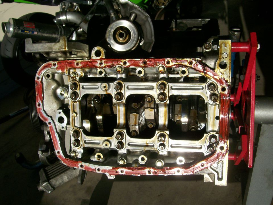 Engine block on red stand, oil pan removed, main girdle exposed with red RTV on pan rail