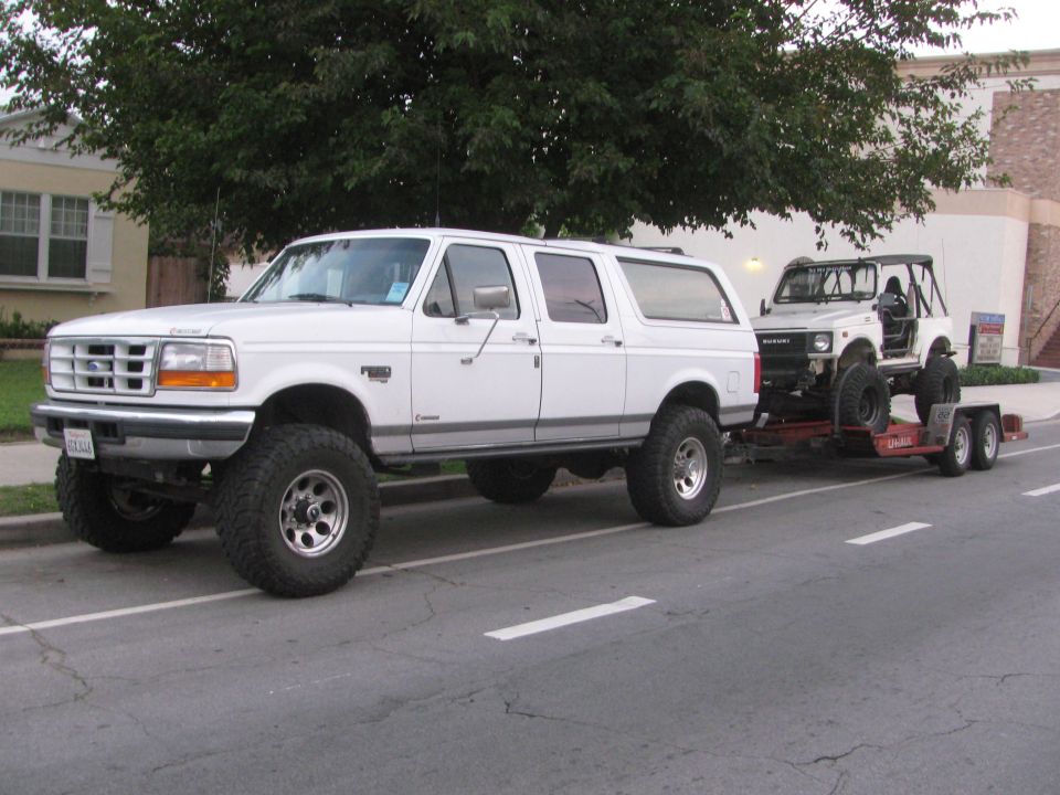 1987 Suzuki Samurai on trailer, white, lifted, off-road tires, towed by white Ford Bronco
