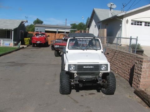 1987 Suzuki Samurai - A white Suzuki Samurai is parked in a driveway with other vehicles behind it under a clear blue sky.