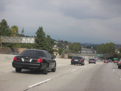 2004 Ford Crown Victoria - Black 2004 Ford Crown Victoria police car on a multi-lane highway under a cloudy sky.