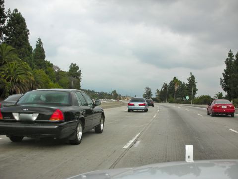 2004 Ford Crown Victoria - A black 2004 Ford Crown Victoria is seen from behind on a highway with other vehicles.
