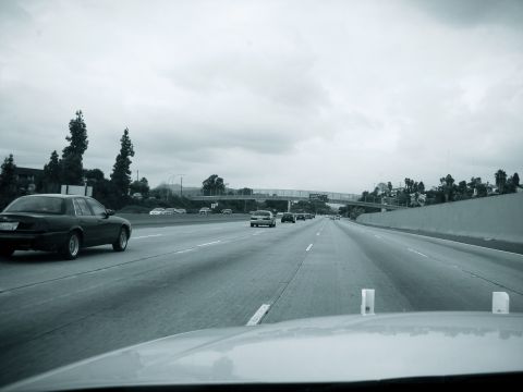 2004 Ford Crown Victoria - A black 2004 Ford Crown Victoria is seen driving on a multi-lane highway under an overcast sky.