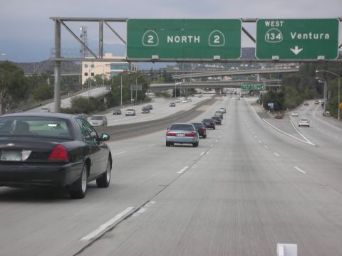2004 Ford Crown Victoria - A black 2004 Ford Crown Victoria is seen from behind on a highway with multiple lanes and other vehicles.