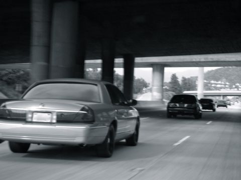 2004 Ford Crown Victoria - Rear view of a silver 2004 Ford Crown Victoria on a highway, with other vehicles visible ahead.