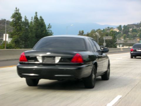 2004 Ford Crown Victoria - Rear view of a black 2004 Ford Crown Victoria sedan driving on a highway.