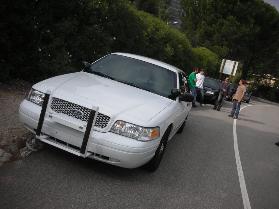 White Ford Crown Victoria with push bumper parked on the side of a road, people standing around it