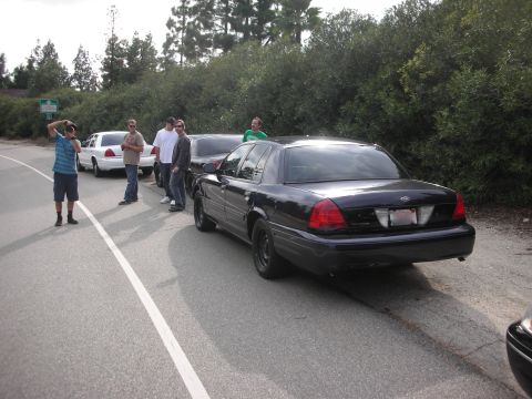 2004 Ford Crown Victoria - A black 2004 Ford Crown Victoria is parked on the side of the road with several people standing nearby.