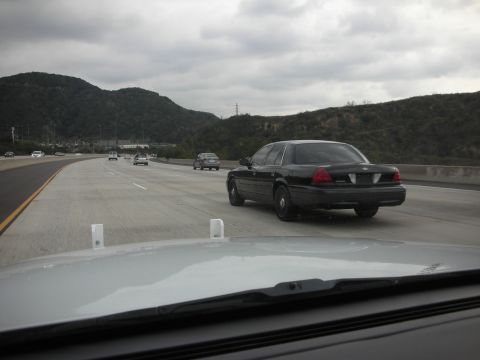 2004 Ford Crown Victoria - A black 2004 Ford Crown Victoria is seen driving on a highway under a cloudy sky.