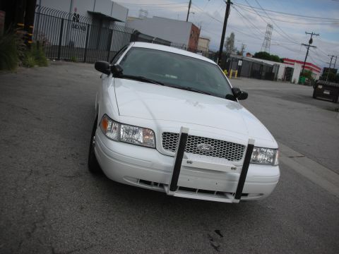 2004 Ford Crown Victoria - A white 2004 Ford Crown Victoria is parked on a street, facing the camera with a push bar on its front grille.