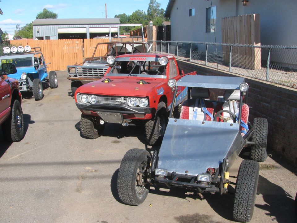 Several off-road project vehicles and a vintage truck parked on a driveway by a fence