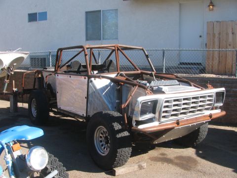 1990 Ford Bronco - unfinished tube-frame off-road truck with bare aluminum panels and a chrome grille sits on a driveway by a fence.