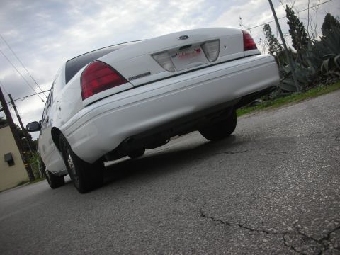 2004 Ford Crown Victoria - The rear of a white 2004 Ford Crown Victoria is shown from a low angle on a cracked asphalt road.