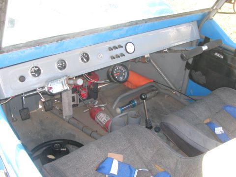 1990 Ford Bronco - Interior of a blue off-road buggy with a painted metal dash, round gauges, floor shifter and a fire extinguisher.