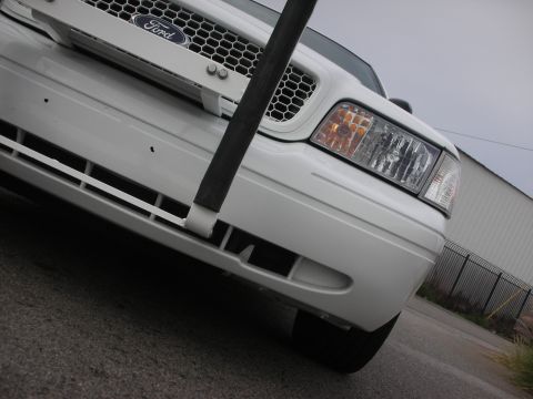 2004 Ford Crown Victoria - A white Ford Crown Victoria's front is captured from a low angle, showing the grille and headlight assembly.