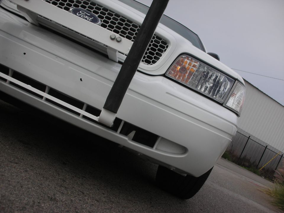 White Ford Crown Victoria front end with a black pole obscuring the grille. Headlight and bumper details are visible