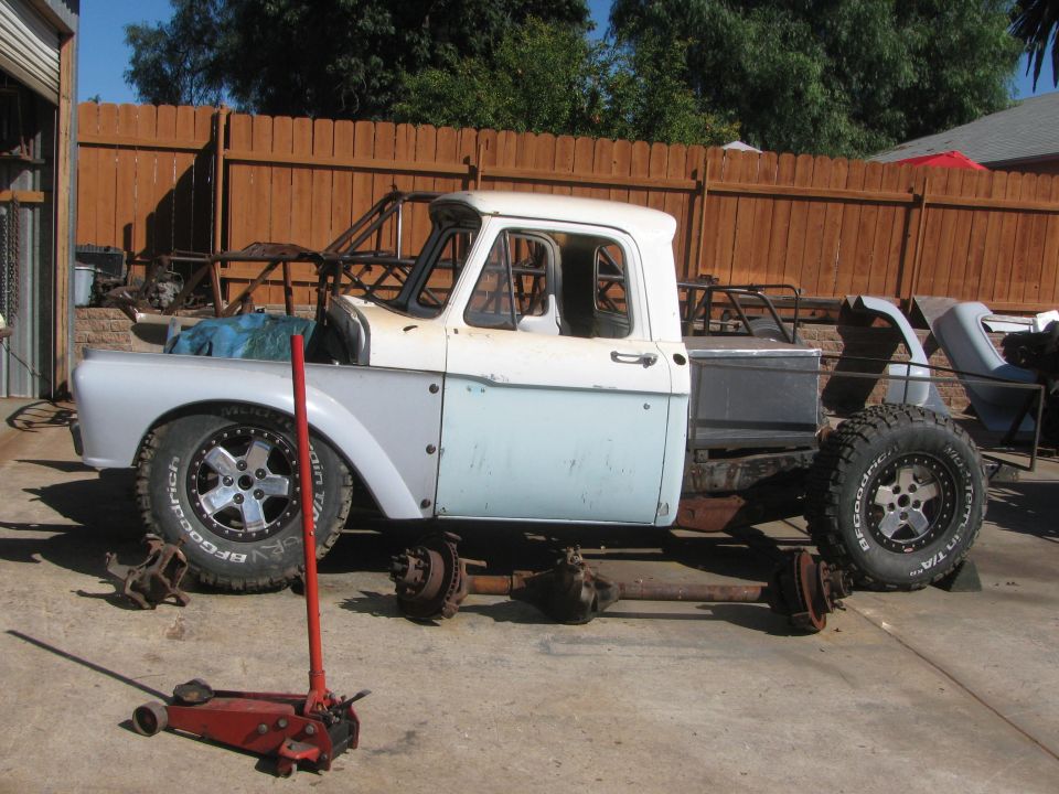 Vintage two-tone pickup cab and bed on axle stands mid-restoration in a yard